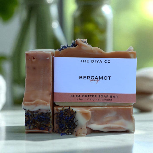 Shea butter soap bar with packaging labeled 'The Diya Co. Bergamot' on a reflective surface with a blurred natural background.