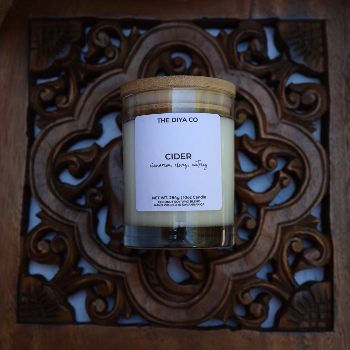 Candle labeled 'Cider' in a decorative wooden frame on a textured surface