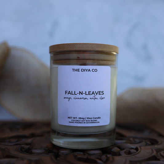 Candle labeled 'Fall N Leaves' by The Diya Co on a textured surface with a blurred background