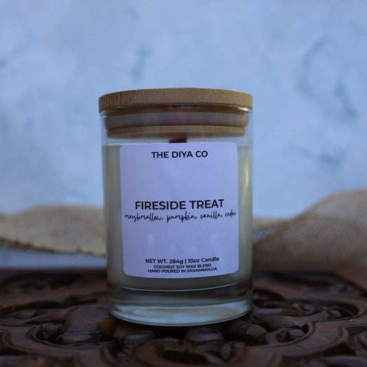 Candle jar labeled 'Fireside Treat' from 'The Diya Co' on a decorative surface with a blurred background.