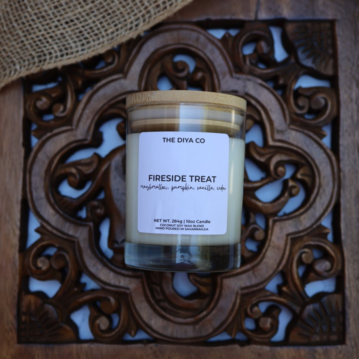 Jar of 'Fireside Treat' candle from The Dya Co on a decorative wooden tray with burlap background