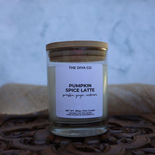 Candle jar labeled 'Pumpkin Spice Latte' from 'The Diya Co' on a textured surface with a blurred background.