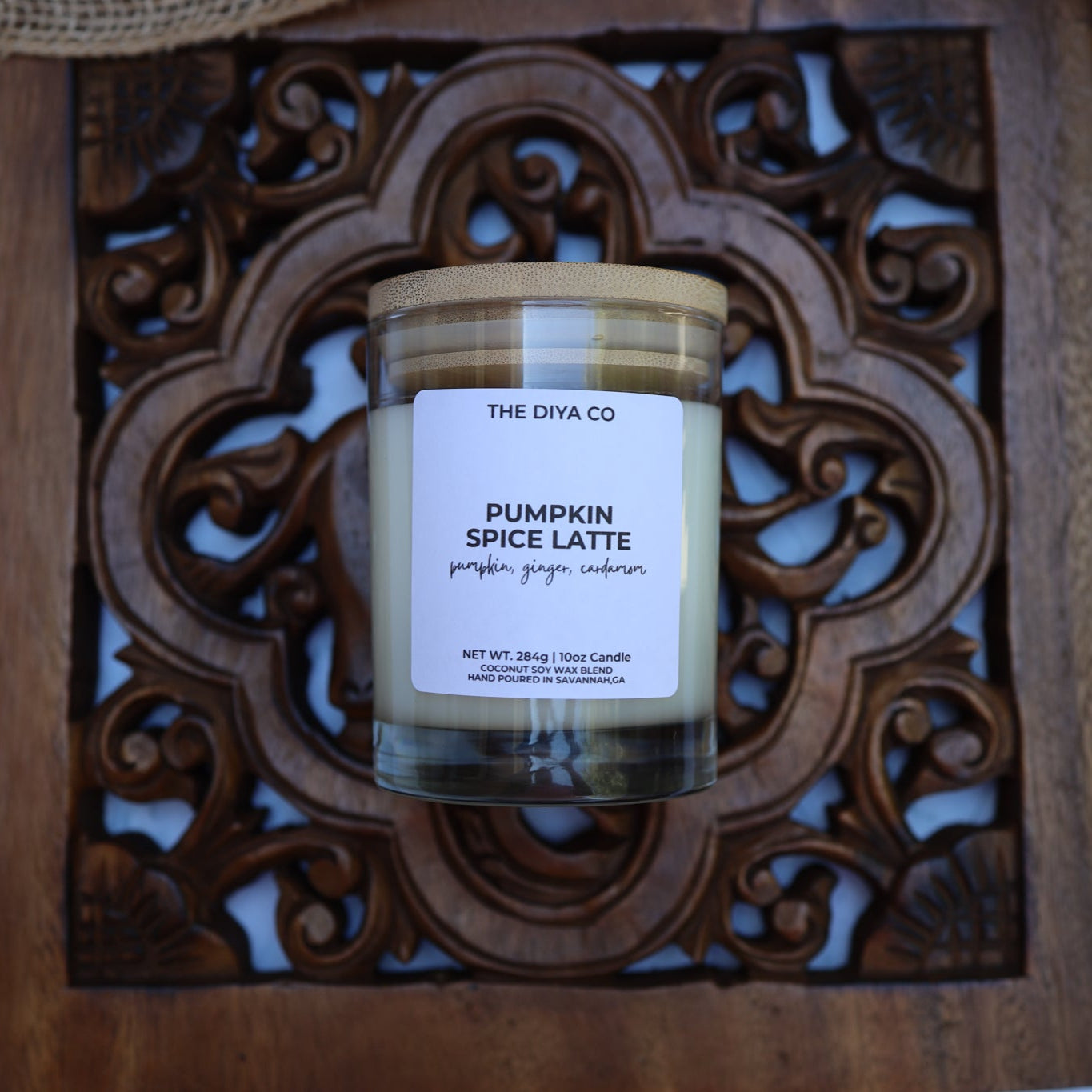 Candle labeled 'Pumpkin Spice Latte' from 'The Diya Co.' on a decorative wooden tray.