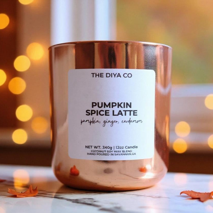 Candle labeled 'Pumpkin Spice Latte' from THE DIYA CO with a blurred background of lights.