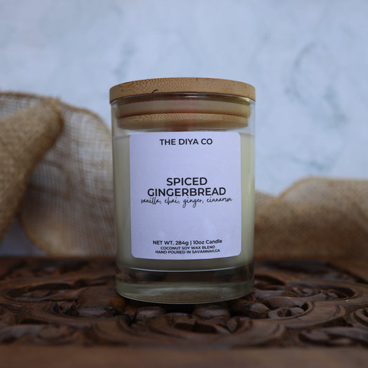 Candle jar labeled 'Spiced Gingerbread' by The Diya Co on a wooden surface with burlap in the background.