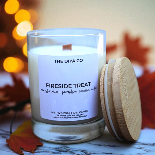 Candle labeled 'The Diya Co' with a wooden lid on a surface with blurred lights and leaves in the background