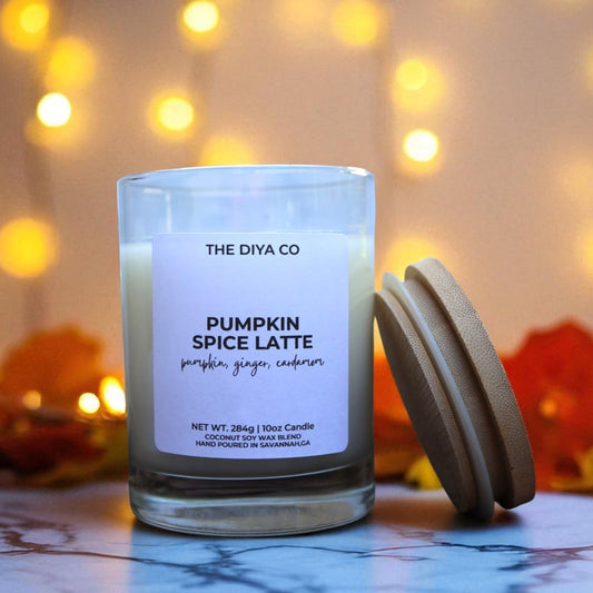 Candle labeled 'Pumpkin Spice Latte' by The Diya Co. with a blurred lights and leaves background.