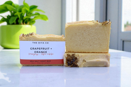 Two soap bars from The Diva Co on a white surface with a plant in the background
