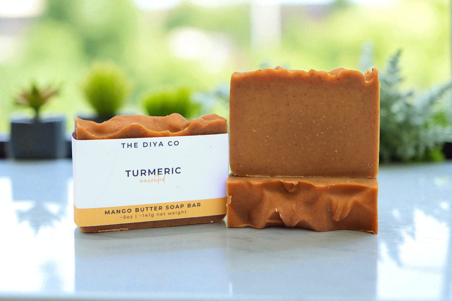 Turmeric soap bar with packaging on a light surface with greenery in the background