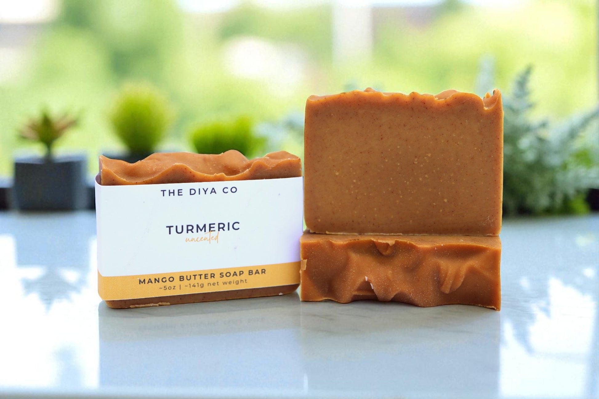 Turmeric soap bar with packaging on a light surface with greenery in the background