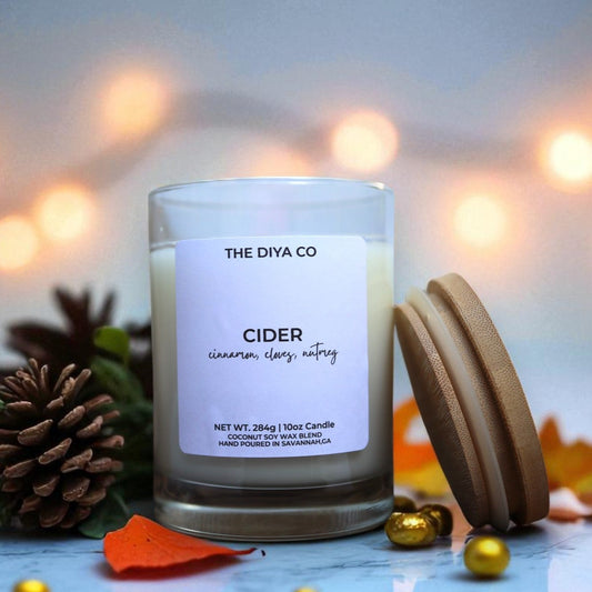 Candle labeled 'Cider' from 'The Diya Co.' with decorative elements on a blurred background