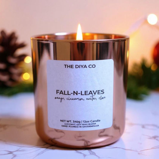 Candle labeled 'The Diya Co. Fall N Leaves' with decorative lights and pinecones in the background